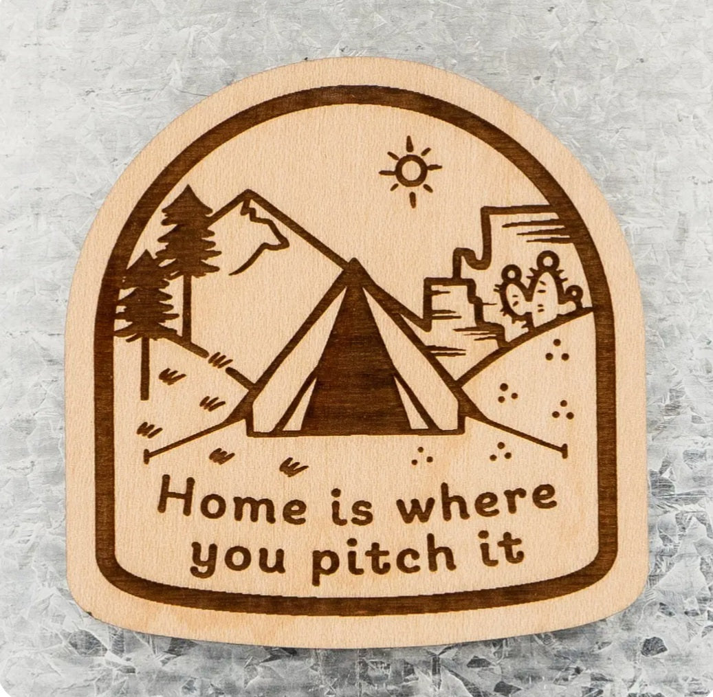 Wood tent-shaped magnet with landscape illustration and text “Home is where you pitch it”