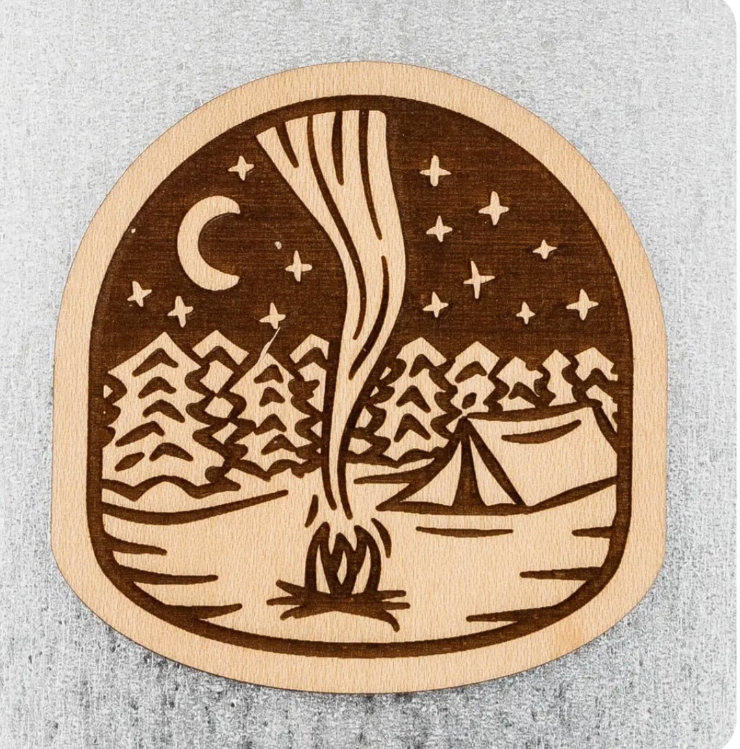 Round campfire wood magnet with night landscape, moon, stars, mountains and tent
