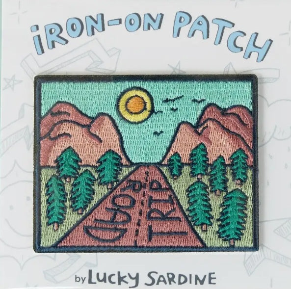 Iron-on patch with turquoise sky, mountains, trees, and a circular planet graphic