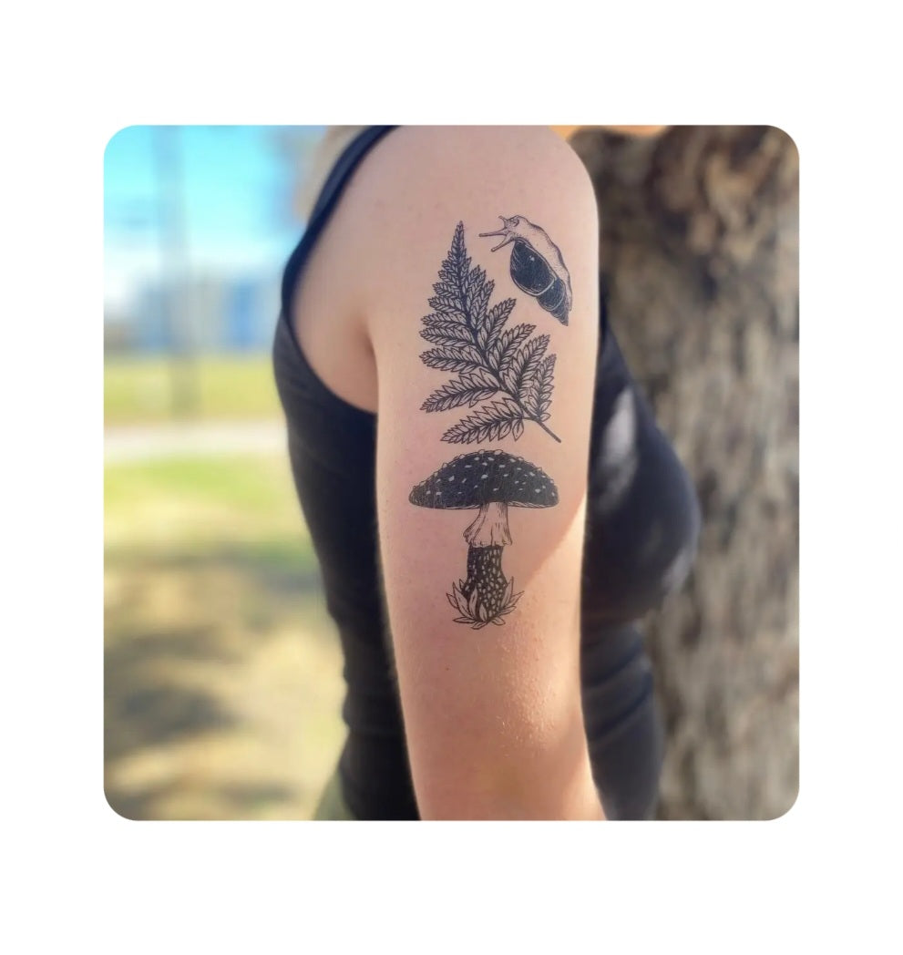 Temporary tattoo on forearm: black fern, mushroom, snail and small bird motifs.