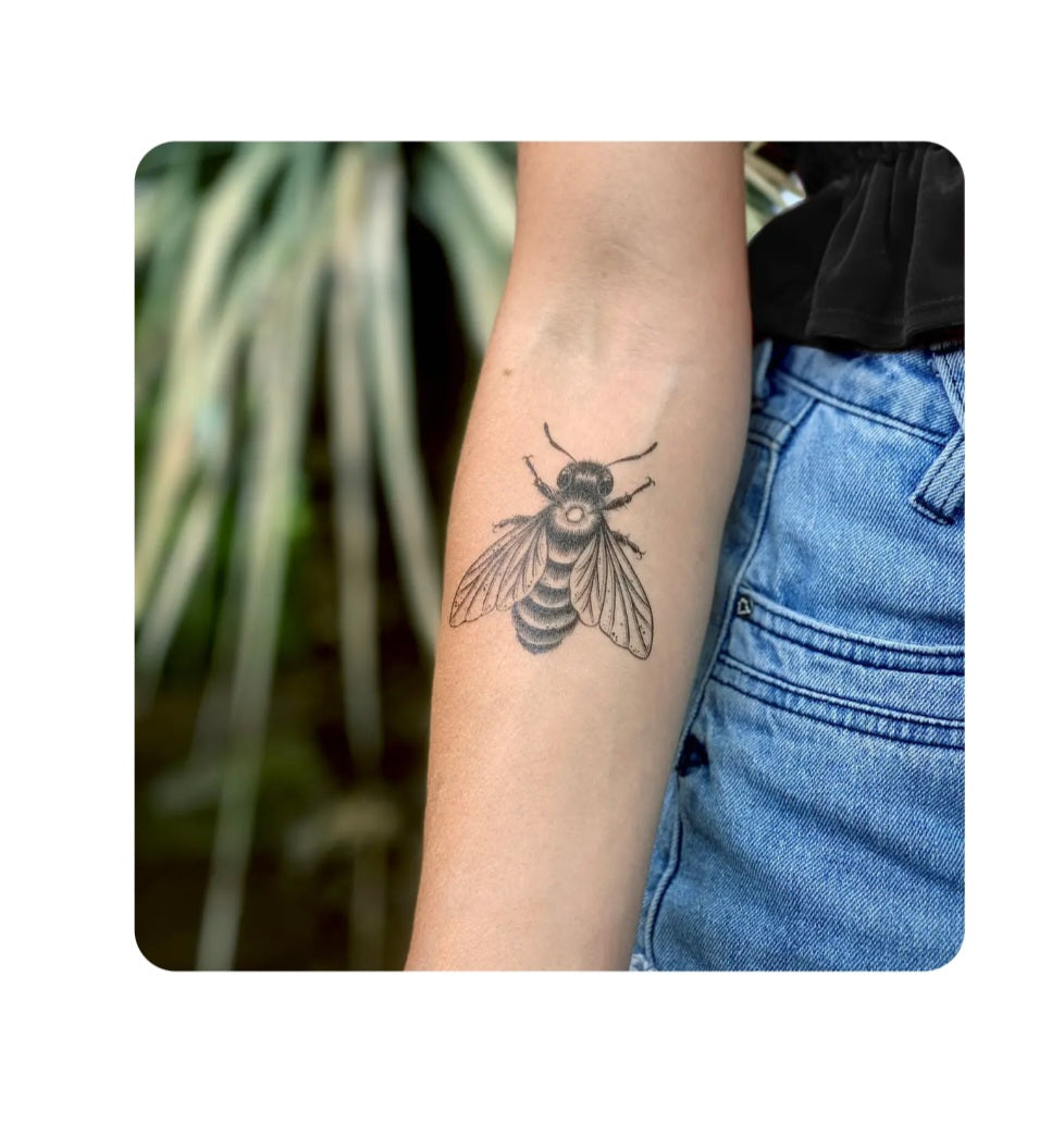 Bee temporary tattoo on forearm, black line art with wings and antennae.