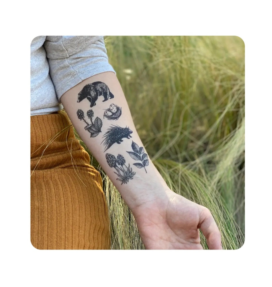 Temporary tattoo on arm with black forest animals and botanical details