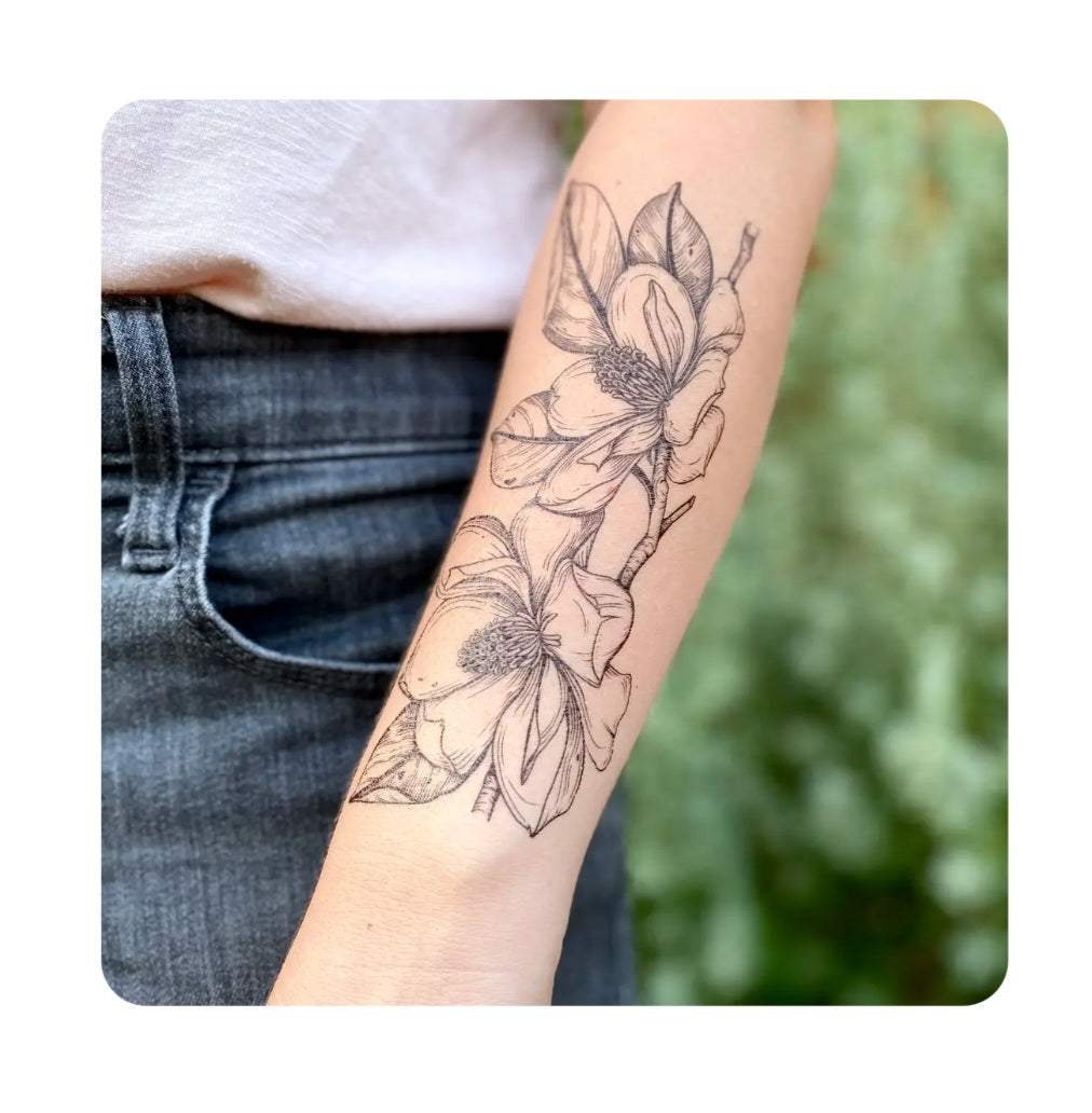 Magnolia flower temporary tattoo on forearm, black botanical line art design