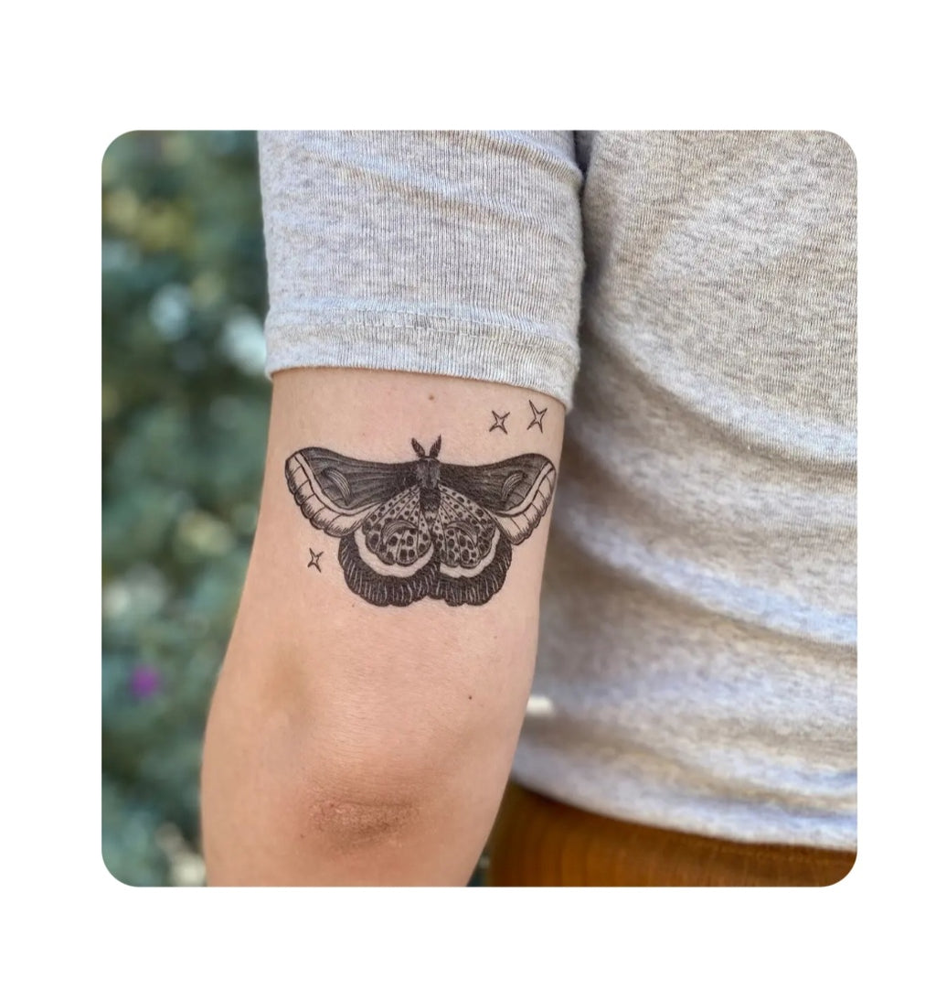 Night moth temporary tattoo on wrist, black ink moth with wings and antennae.