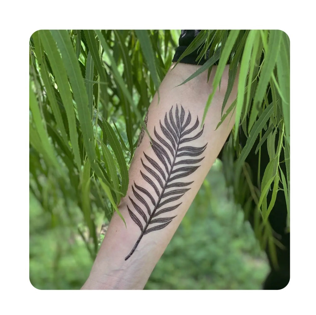 Palm leaf temporary tattoo on forearm, black botanical leaf design