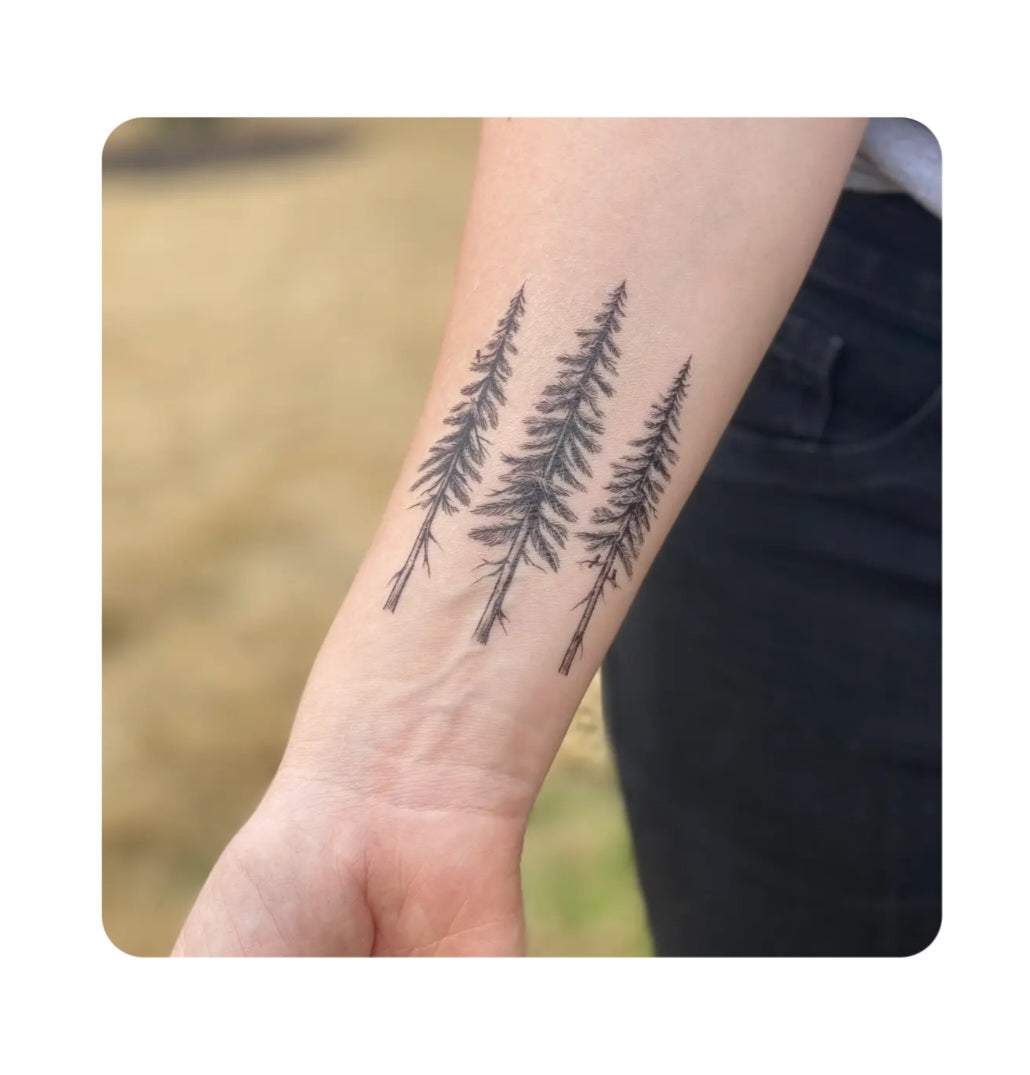 Pine tree temporary tattoo on forearm, three dark pine silhouettes