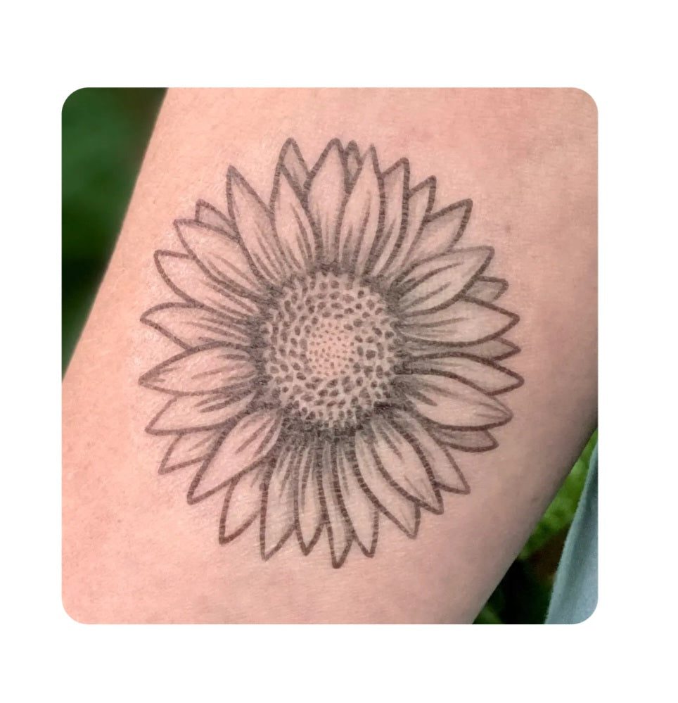 Sunflower temporary tattoo on skin, detailed black outline with dotted center.