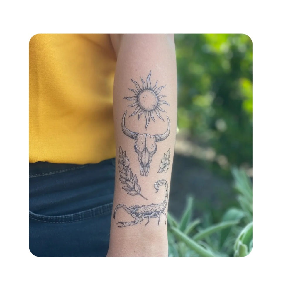 Temporary tattoo with sun, bull skull, scorpion, and leaves on forearm