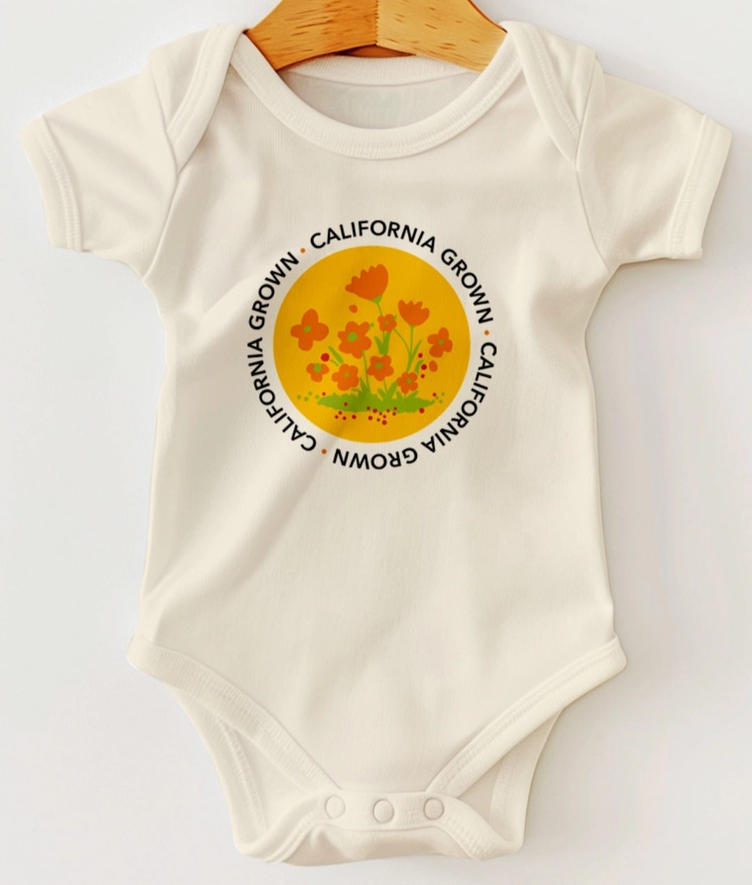 Ivory baby onesie with short sleeves and round floral logo graphic on front