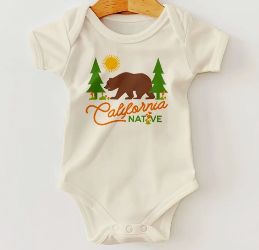 Ivory baby onesie with short sleeves and bear, pine trees, and California Native graphic